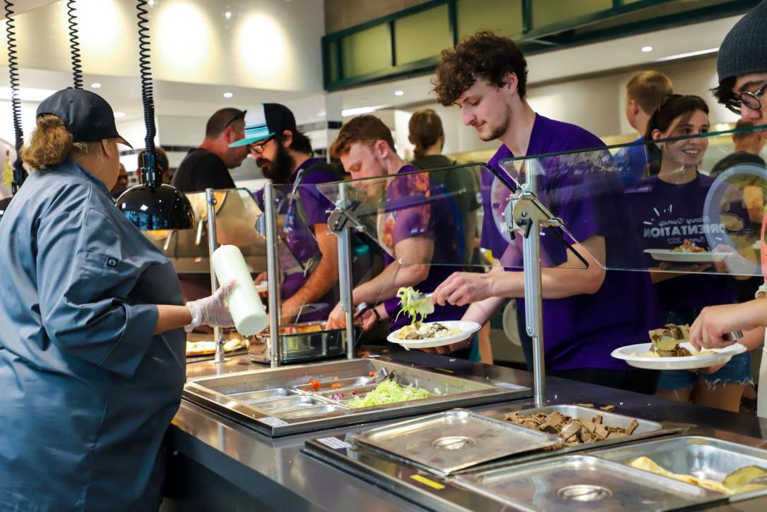 Kettering students add food to their plates from a buffet line in Battenberg Cafe. A cafeteria worker helps serve them.